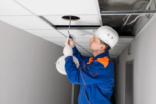 an electrician installing lighting in a false ceiling, side view