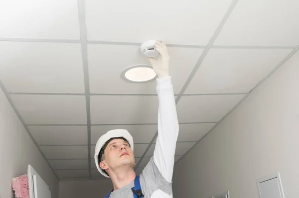 a worker installs a fire safety sensor on a suspended ceiling