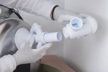 Koruyucu eldivenlerde uzman biri, metal bir lavaboya beyaz bir kanalizasyon borusu yerleştirir ve toplar.