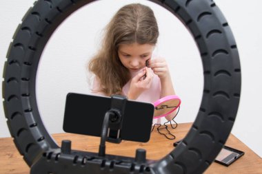 Dairesel lamba ve akıllı telefonun ortasında bir kız blogcu makyaj yapar.