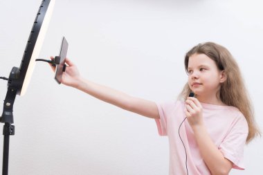 Kız blogcu, dairesel ışığın önünde, mikrofonun sesini kontrol eder ve akıllı telefonu ayarlar, yayından önce.