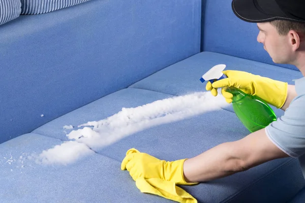 a cleaning service man applies a sofa upholstery cleaner