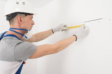 Bir işçi duvardaki delikler arasındaki mesafeyi ölçer.