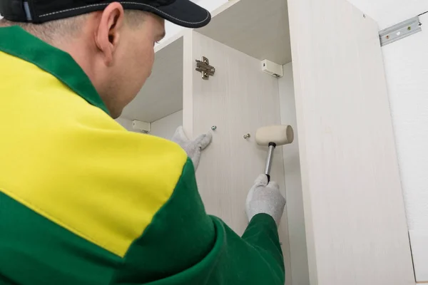 Kitchen furniture assembler assembles the top cabinets with a rubber mallet