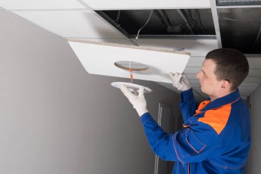 Adam sahte tavanda ışıklandırma onarımı yapıyor, yakın plan.