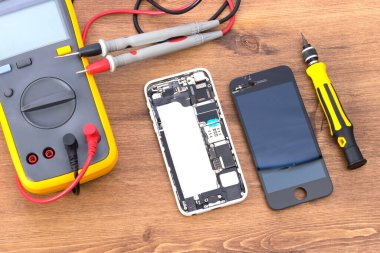 Tahta bir masada elektrikli bir test cihazı ve yerine sıvı kristal ekran olan bir telefon var.