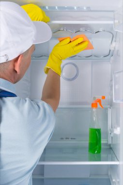 Buzdolabını temizliyor, adam dezenfeksiyon yapıyor, koruyucu eldivenler giyiyor.