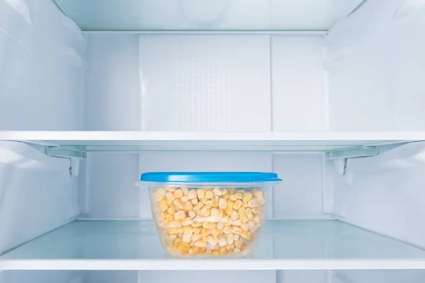 corn kernels in a plastic container, standing on the shelf of the refrigerator, on a white background