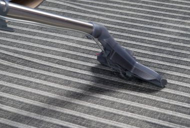 Çizgili gri bir halının arka planında, ıslak temizlik için elektrikli süpürge fırçası, yakın plan.