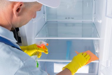 Buzdolabını temizliyor, adam cam rafları sprey ve paçavralarla dezenfekte ediyor.