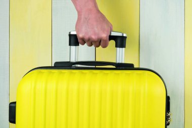 Eller sarı bir valizin sapını tutuyor, yakın plan.