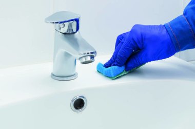 Bir temizlik şirketinin çalışanı musluğu temizliyor ve yıkıyor.