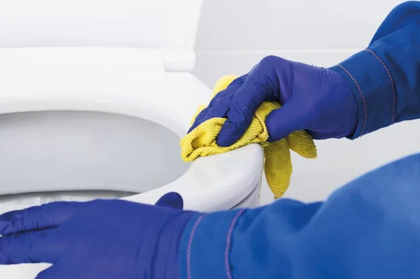 an employee of a cleaning company is cleaning and washing the rim of the toilet bowl, close-up