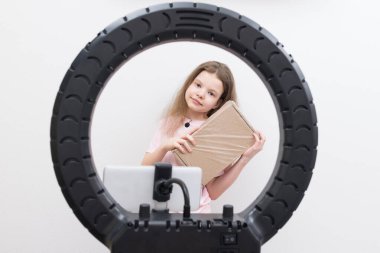 Elinde mikrofon, merkezinde yuvarlak lamba ve akıllı telefon olan blogcu bir kız paketleri açmak için gözden geçirir.