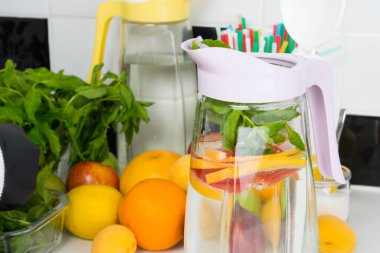 İçeceklerin arka planına karşı, ferahlatıcı bir içecekte ince doğranmış meyve dolu bir sürahi yakın plan.