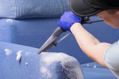 Elektrikli süpürge fırçası mavi kanepeden köpük topluyor, temizlik şirketi çalışanı.