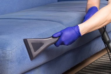 Kirli bir mavi kanepeyi elektrikli süpürgeyle temizliyorum.