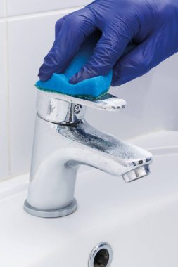 Bir temizlik şirketinin çalışanı musluğu temizliyor ve yıkıyor.