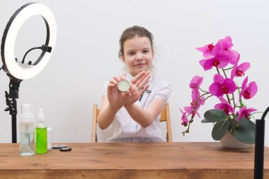 Video çekim ekipmanlarıyla çevrili bir blogcu kız, bir yüzük lambası ve akıllı telefon tutucusu, üretici tarafından sipariş edilen dudak parlatıcısını gözden geçirir.