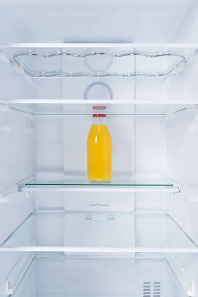 glass bottle with orange juice, in the refrigerator on the shelf, on a white background