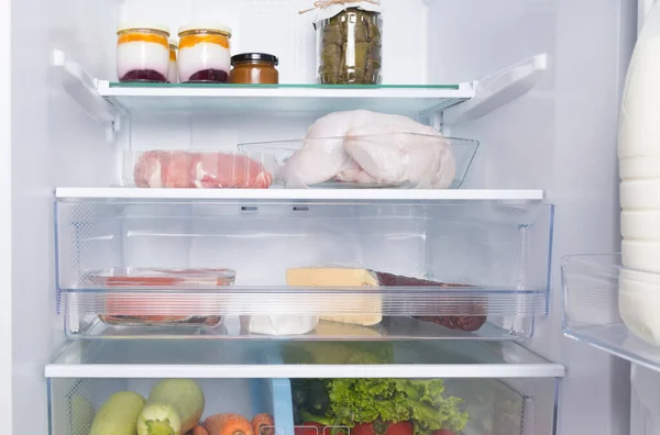 on glass shelves and drawers, in a white refrigerator, there are products, whole chicken, meat, fish, sausage, cottage cheese, yogurt and fresh vegetables