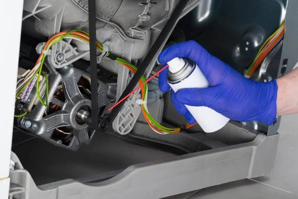 Elin WD-40 ile yakın plan çamaşır makinesi sürücünün hareket eden parçalarını tamir ederken