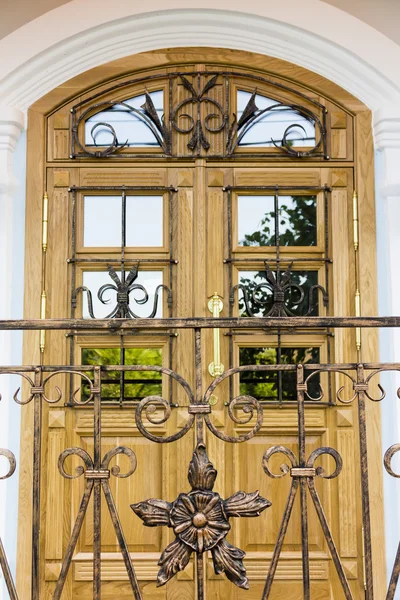 Une porte d'entrée en bois d'une maison familiale en grès brun. La porte est encadrée par une arche, des balustrades jumelles et des pots de fleurs . — Photo