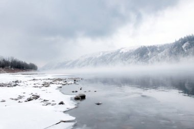 Kış ayaz manzarası, beyaz ormanların arasındaki sisli nehir, kayalık kıyıdan manzara. Peace River, Alberta, Kanada.