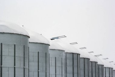 Soğuk kış mevsiminde tohum depolayan tarım çeliği kutuları. Çiftlikte ve kar yağdıktan sonra tahıl ambarlarında kar yığınları. En küçük monokrom fotoğrafı.