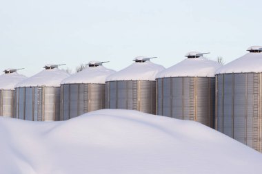 Soğuk kış mevsiminde tohum depolayan tarım çeliği kutuları. Çiftlikte ve kar yağdıktan sonra tahıl ambarlarında kar yığınları. Sabah yumuşak ışıkta en az.