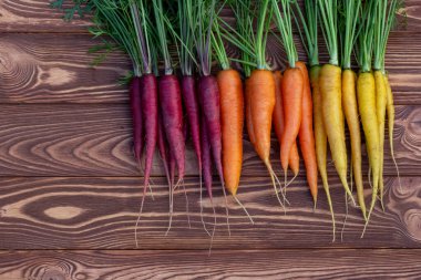 Kahverengi ahşap masanın üzerinde yeşil yapraklı renkli organik sarı, kırmızı ve turuncu havuç (Gökkuşağı karışımı) demeti bulunmaktadır. Taze sonbahar mahsulü.