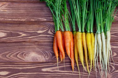 Renkli sarı ve turuncu havuçlar (Gökkuşağı karışımı) ve yeşil yapraklı beyaz (Luna beyaz çeşitliliği) kahverengi ahşap masanın üzerindedir. Taze sonbahar mahsulü.