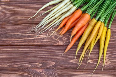 Renkli sarı ve turuncu havuçlar (Gökkuşağı karışımı) ve yeşil yapraklı beyaz (Luna beyaz çeşitliliği) kahverengi ahşap masanın üzerindedir. Taze sonbahar mahsulü.