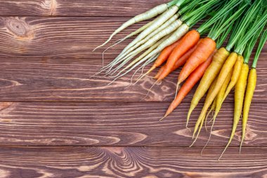 Renkli sarı ve turuncu havuçlar (Gökkuşağı karışımı) ve yeşil yapraklı beyaz (Luna beyaz çeşitliliği) kahverengi ahşap masanın üzerindedir. Taze sonbahar mahsulü.