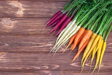 Renkli sarı, kırmızı ve turuncu havuçlar (Gökkuşağı karışımı) ve yeşil yapraklı beyaz (Luna beyaz çeşitliliği) kahverengi ahşap masa üzerindedir. Taze sonbahar mahsulü.