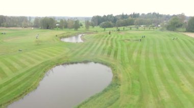 Sigulda, Latvia - October 7, 2025 - Aerial footage of a golf course with visible fairways, sand bunkers, ponds, and golfers playing under cloudy skies in a scenic countryside landscape.