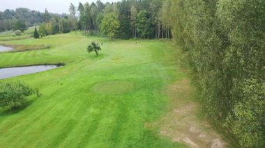 Sigulda, Latvia - October 7, 2025 - Aerial view of a golf course, showing the full hole from tee to green, with golfers walking under umbrellas and a scenic landscape surrounding the fairway.