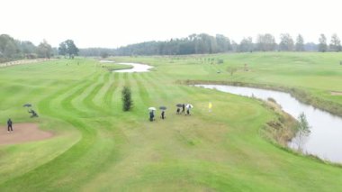 Sigulda, Latvia - October 7, 2025 - Aerial footage of a golf course with visible fairways, sand bunkers, ponds, and golfers playing under cloudy skies in a scenic countryside landscape.