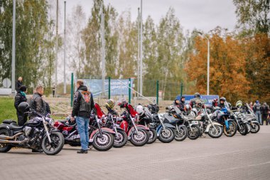 Valmiera, Latvia - October 4, 2025 - Group of motorcyclists gathered in a parking area with a line of various motorcycles. People are chatting and preparing for a ride on an overcast day.