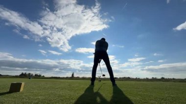 Otepa, Estonya - 02 Ekim 2025: Mavi gömlekli golfçü yeşil alanda sallanmaya hazır, kamera aksiyon sahnesini yakalamak için sorunsuz tavalar