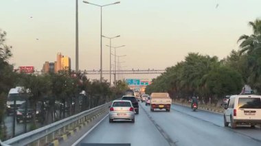 Kemer, Türkiye - 24 Eylül 2025: Şehir trafik sahnesinde palmiye çizgili bir yolda ilerleyen araçlar görülüyor, kameralar pürüzsüz bir hareketle takip ediliyor