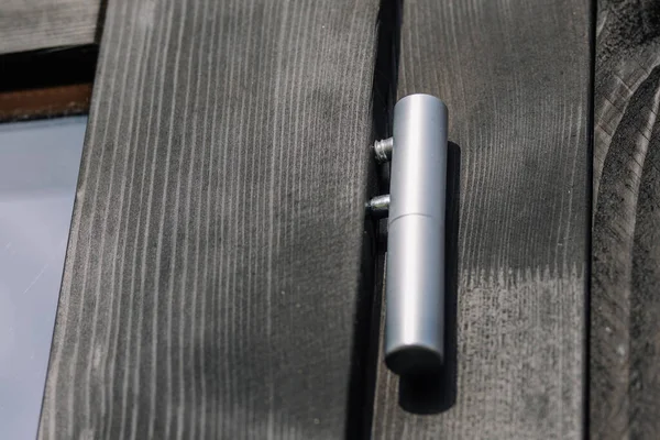 Close-up of a metallic silver hinge mounted on a black wooden surface, showing detailed texture of wood grain and modern hardware under natural light.