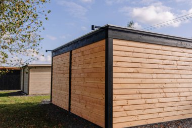 Close-up side view of a modern wooden garden house with light timber siding and black trim, captured under clear skies in a rural outdoor setting.