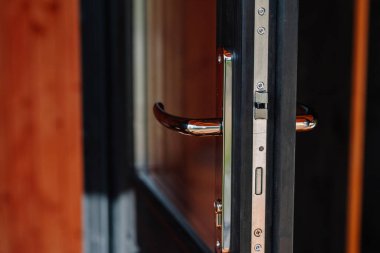 Close-up of a modern chrome door handle and metal latch mechanism on a partially open black wooden and glass door, showing hardware detail and sleek design.