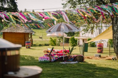 Saldus, Latvia - July 19, 2025 - Bohemian-style chill zone at a hippie festival with hay seating, colorful fabric, parasols, streamers, and outdoor decor on a sunny summer day.