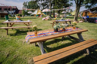 Saldus, Latvia - July 19, 2025 - Outdoor picnic tables decorated with colorful hippie-style runners and fresh flowers at a summer festival surrounded by tents and festive decorations.