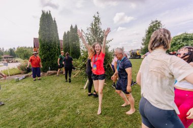 Saldus, Latvia - July 19, 2025 - Joyful woman raises her hands celebrating during a fun water activity at a hippie festival. People around are wet, smiling, and enjoying the summer outdoors.