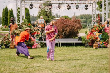 Saldus, Latvia - July 19, 2025 - Colorfully dressed performers entertain on stage at a hippie festival surrounded by flowers, decorations, and a lively summer atmosphere in the countryside.
