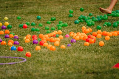 Bright, colorful plastic balls scattered on a grassy field with a barefoot person jumping into the frame. Likely part of an outdoor game or festival activity.