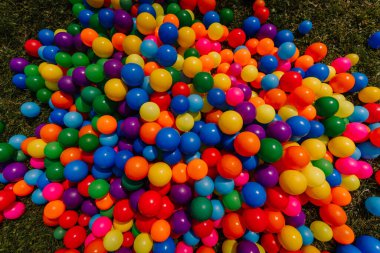A vibrant pile of colorful plastic balls on the grass, typically used for kids play or event decorations. Bright, cheerful, and eye-catching